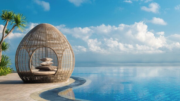 A spherical wicker chair with cushions by a poolside, palm trees, and a clear blue sky. - Renaissance Bali Uluwatu Resort & Spa (Ungasan)