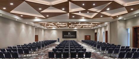 A conference room with rows of chairs, a patterned carpet, and a geometric ceiling design.