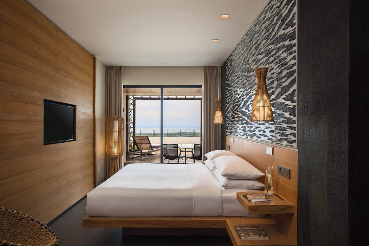 A modern hotel room with a large bed, a TV, a balcony with seating, and a unique wall design.