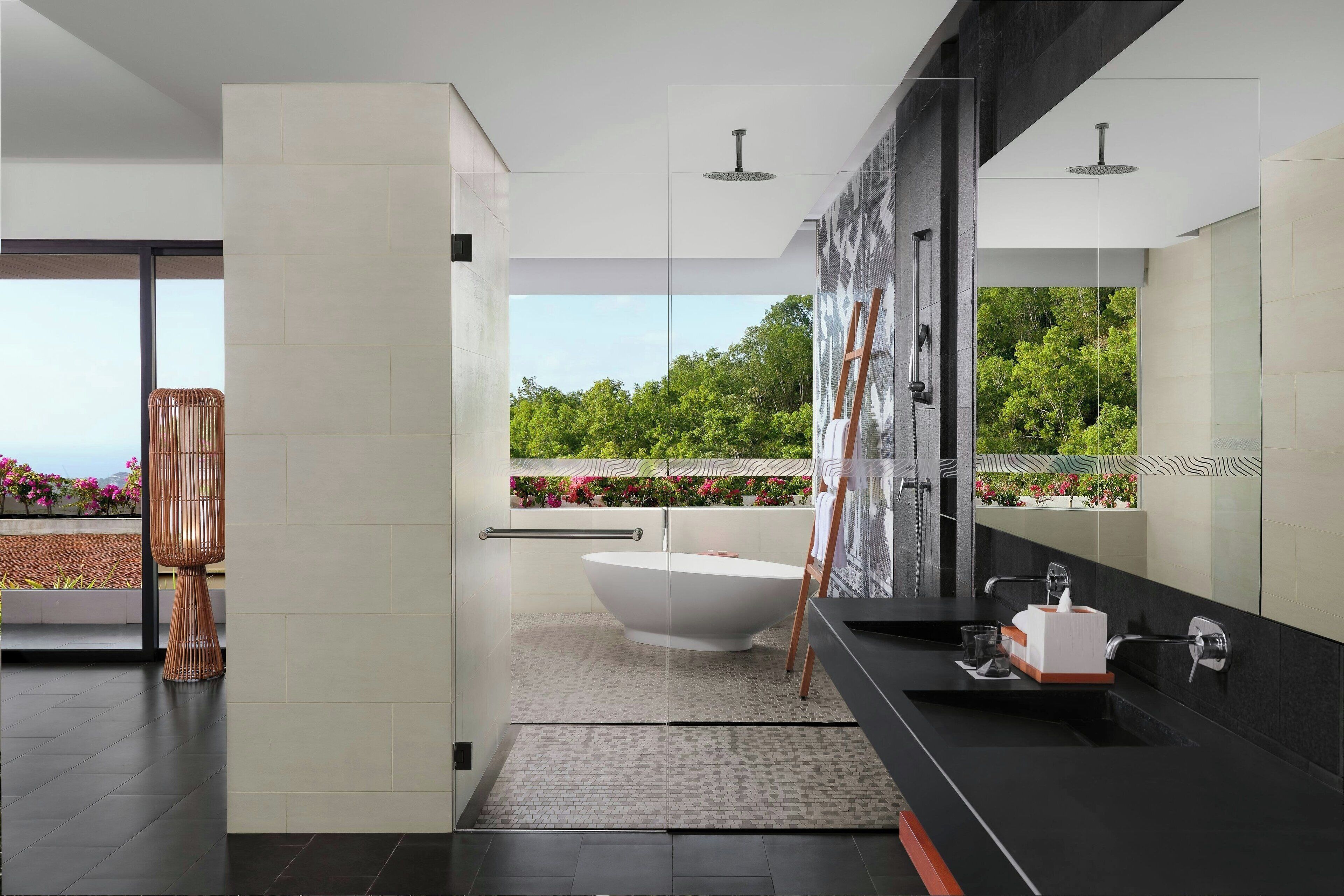 Une salle de bain moderne avec une baignoire sur pieds, un grand miroir et une vue sur la verdure environnante.