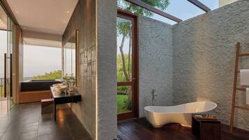 Un baño moderno con una bañera independiente, un banco de madera y un amplio ventanal con vistas a la vegetación.