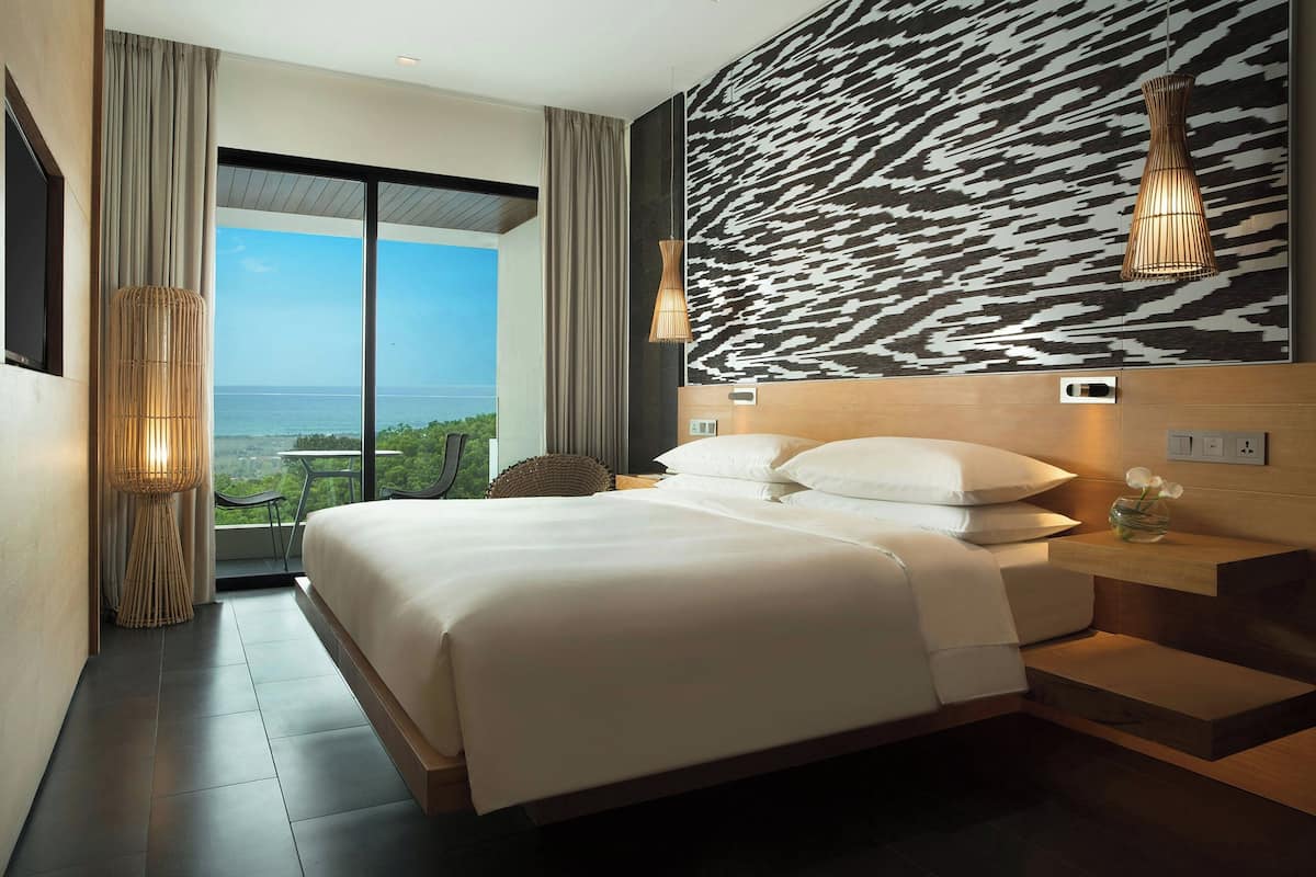A modern hotel room with a large bed, a view of the sea, and a unique patterned wall.