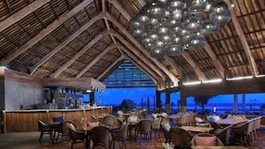 A restaurant with a high wooden ceiling and hanging spherical lights. Tables and chairs are arranged for dining. - Renaissance Bali Uluwatu Resort & Spa (Ungasan)