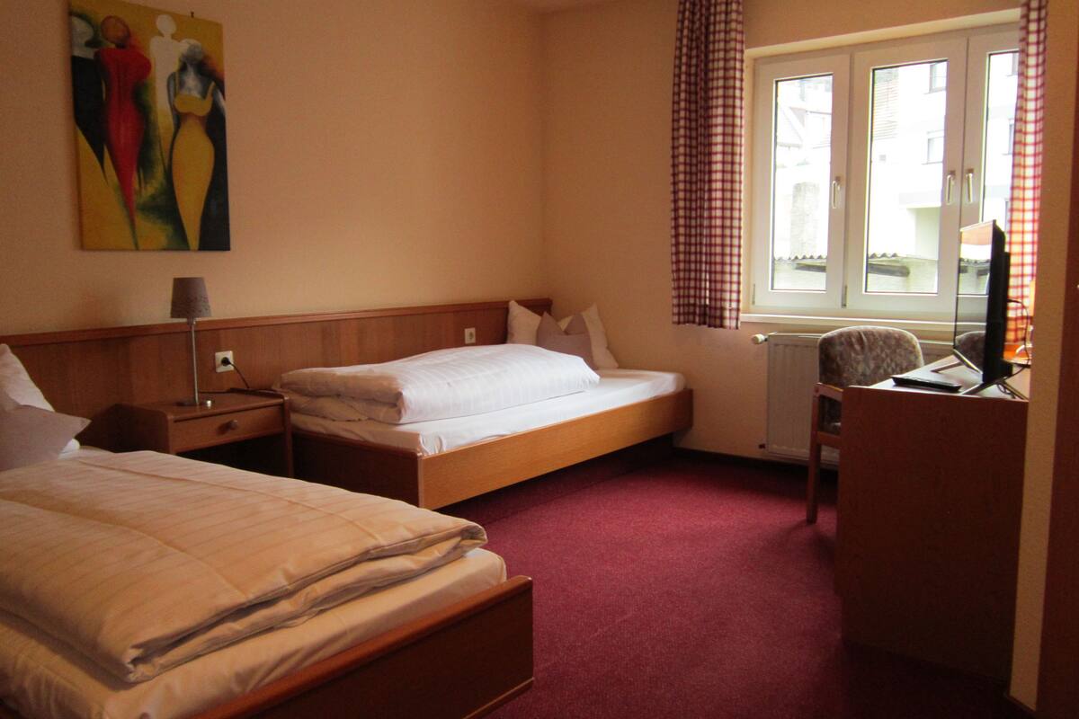 A hotel room with two beds, a desk with a computer, a window with curtains, and a painting on the wall.