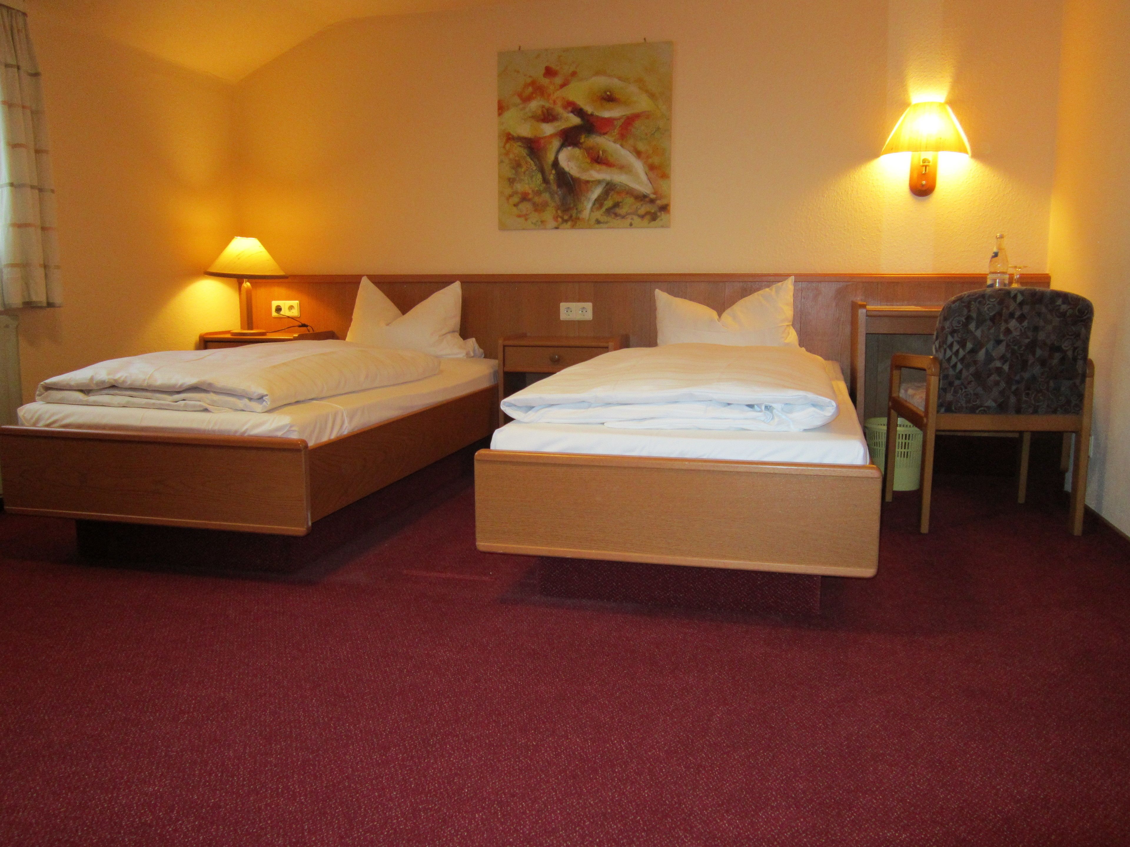 A hotel room with two beds, a desk, a chair, and a painting on the wall.