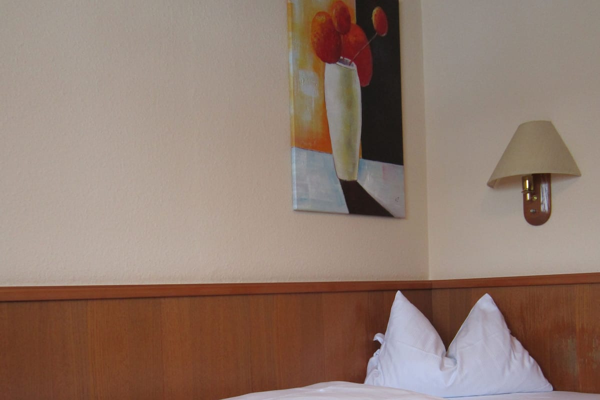 A hotel room with a wooden headboard, a single bed with white linens, and a painting of fruit on the wall.