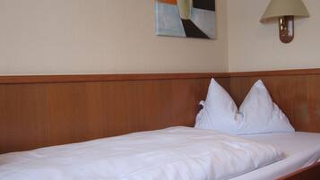 Une chambre d’hôtel avec une tête de lit en bois, un lit simple avec du linge de lit blanc et un tableau représentant des fruits accroché au mur.