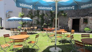 An outdoor seating area with tables and chairs under blue umbrellas, a stone wall, and a door in the background. - Gasthaus Neupert (Lemberg)