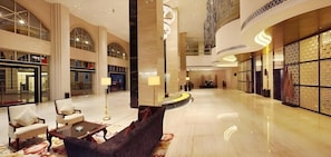 A spacious lobby with a reception desk, seating area, and a large decorative column. - Yihe Grand Hotel (Zhongshan)
