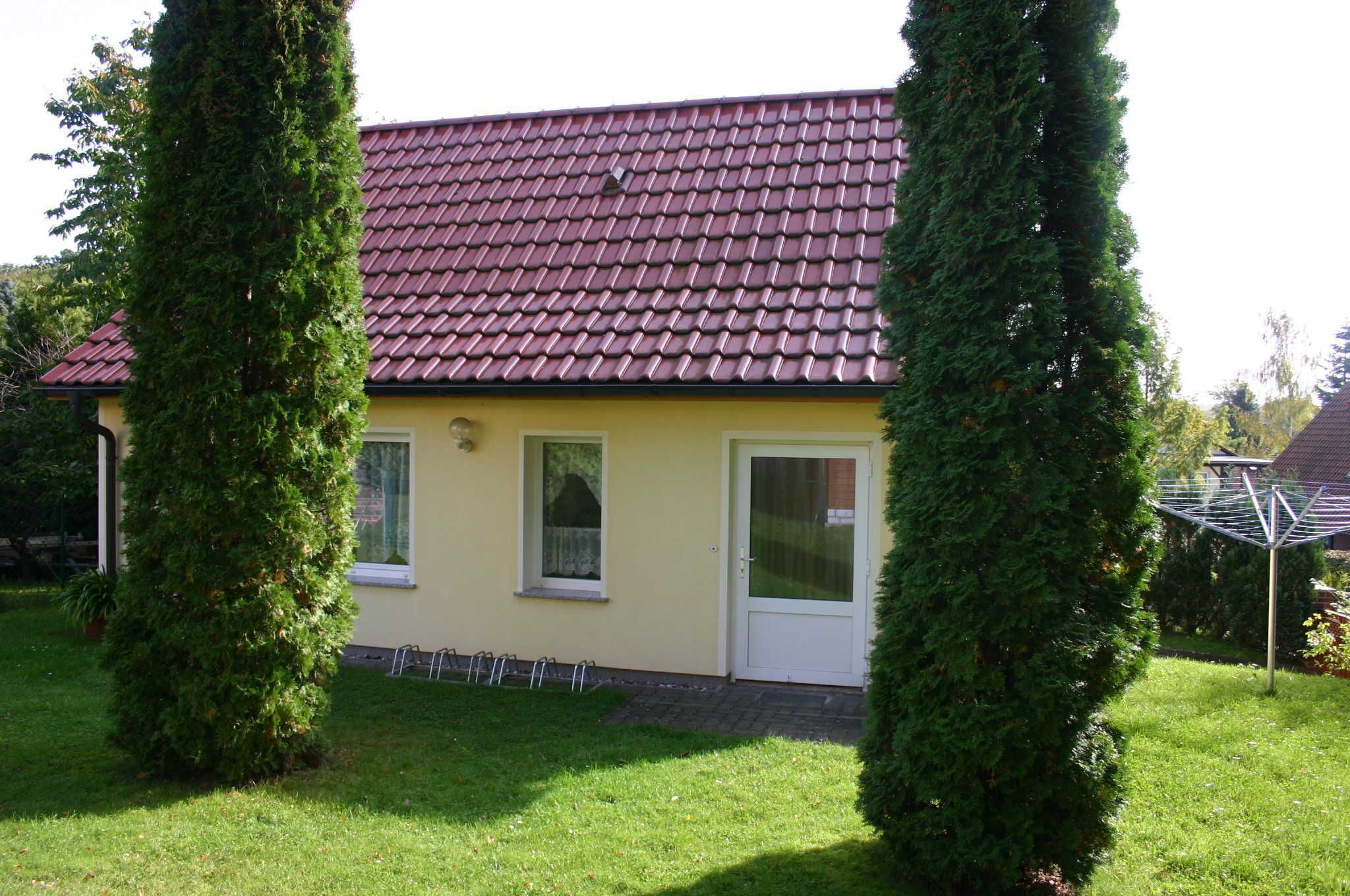 Ein gelbes Haus mit einem roten Ziegeldach, umgeben von grünen Hecken.