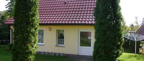 A yellow house with a red-tiled roof, surrounded by green hedges.