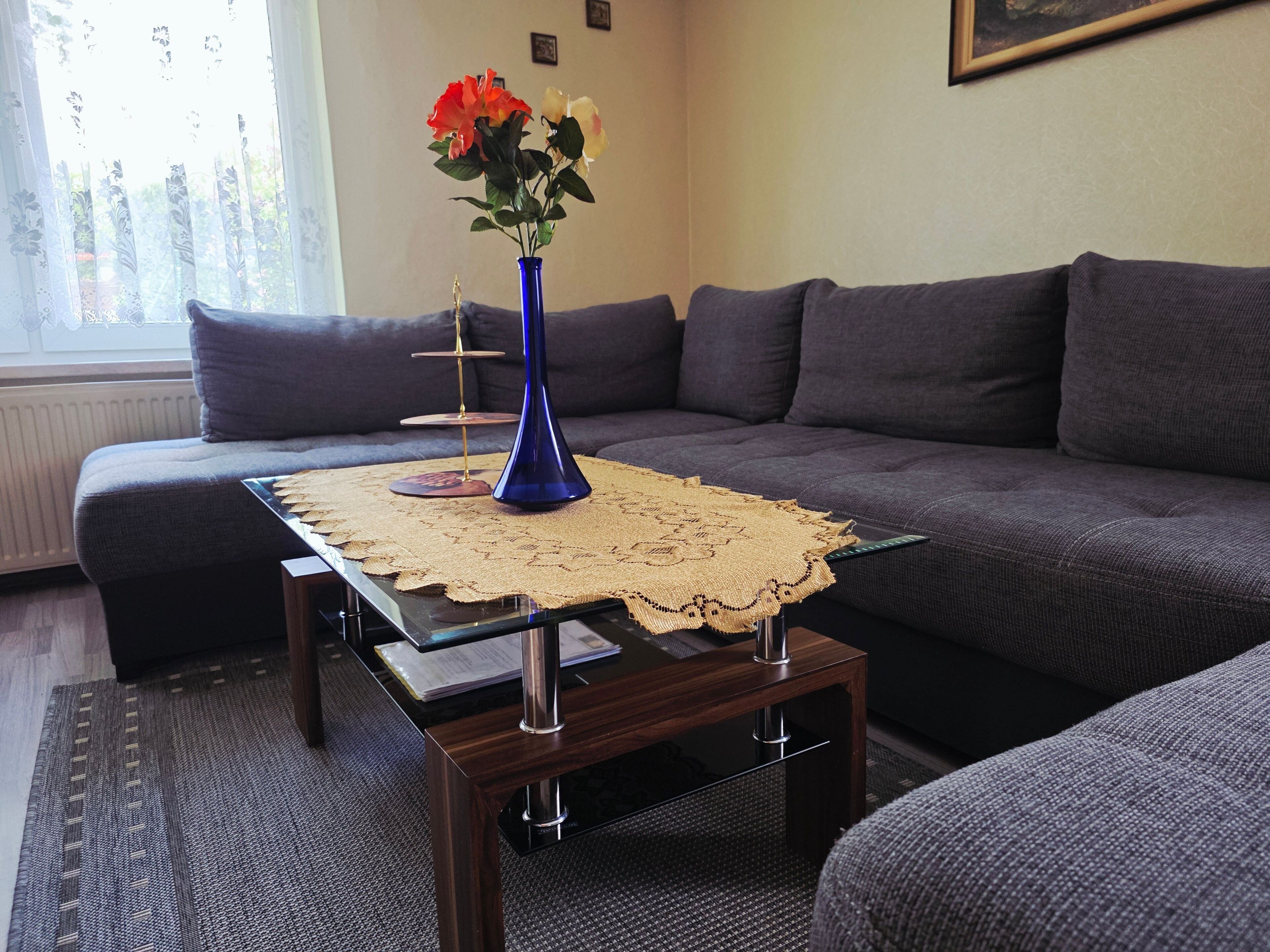 Ein Wohnzimmer mit einer Couch, einem Couchtisch mit Unterlage und einer Vase mit Blumen.