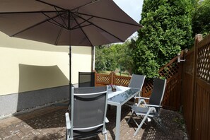 An outdoor patio with a table and chairs, a large umbrella, and a wooden fence.