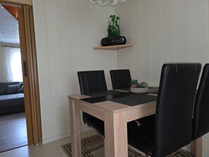 En matplats med ett träbord, svarta stolar, en liten hylla med en växt och en högtalare.