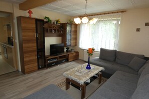 A living room with a sofa, TV, wooden cabinet, and a vase with flowers.