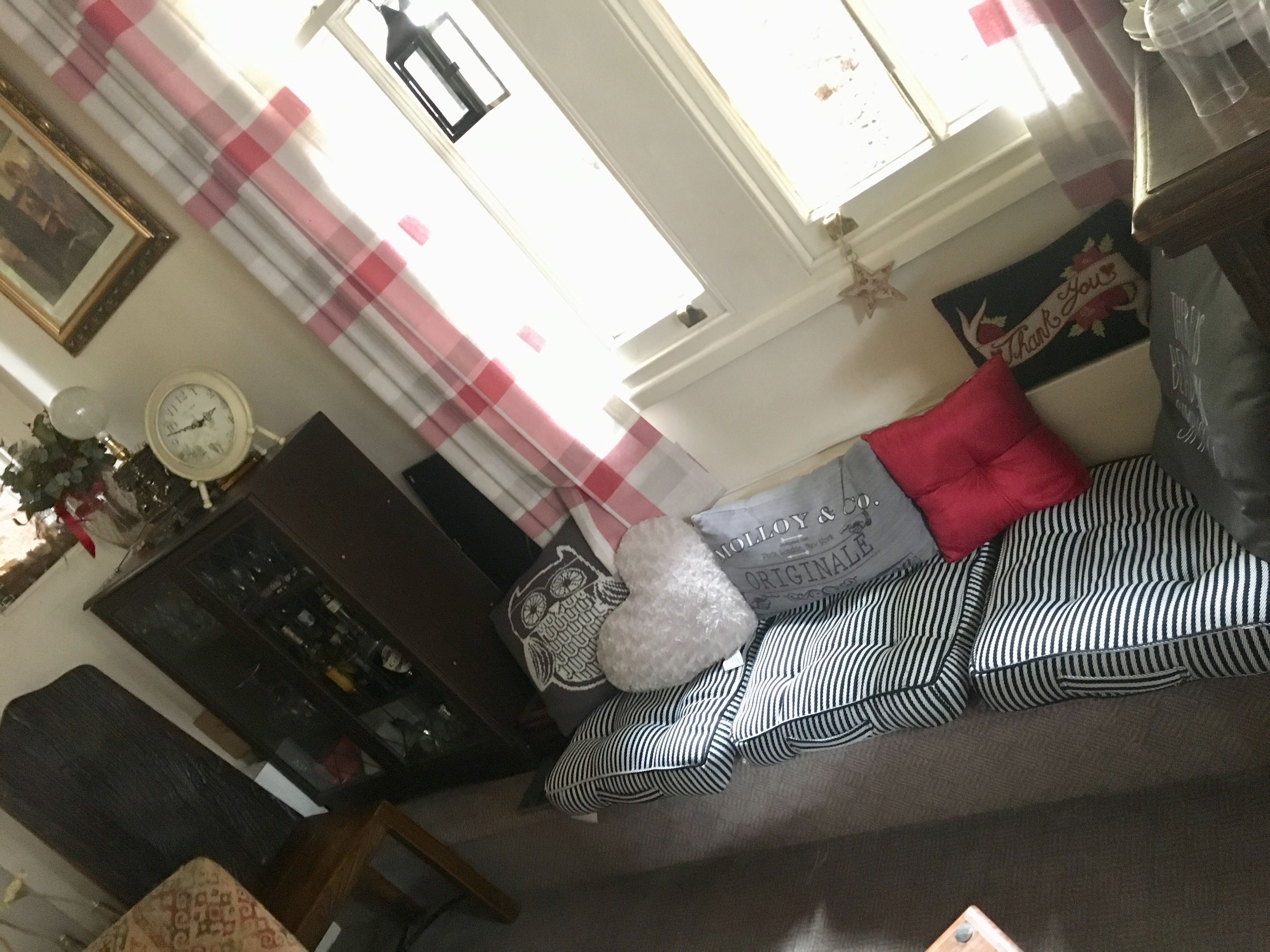 Un salon avec un canapé, des coussins, une horloge, une lampe et une fenêtre avec des rideaux.