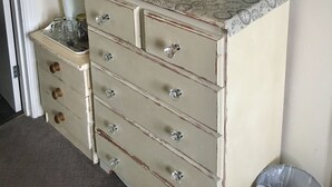 A vintage dresser with a clock pattern top, a mirror with an ornate frame, and a vase with flowers. - Stoneway Guest House (Bridgnorth)