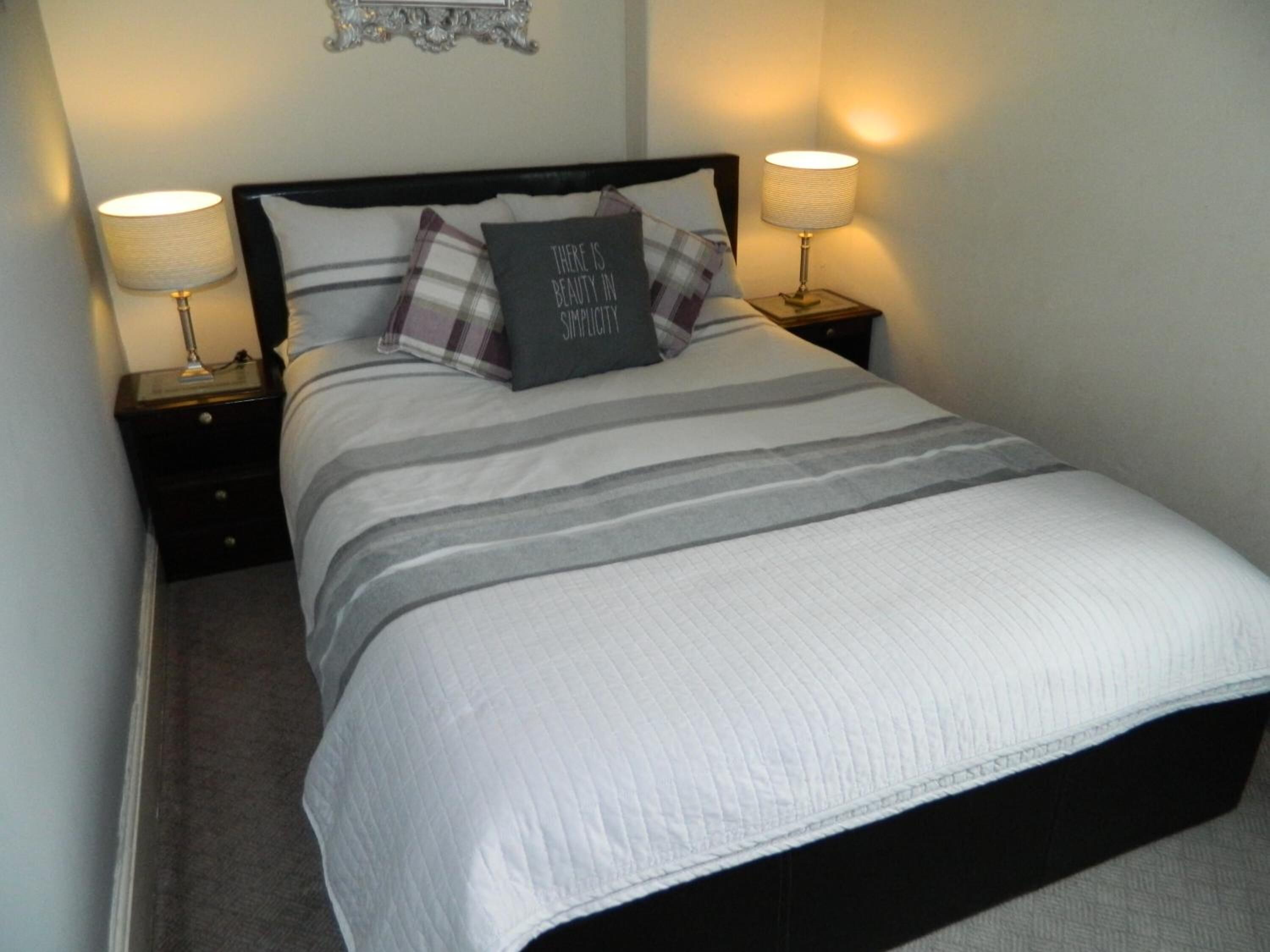 A neatly made bed with a striped bedspread, two bedside lamps, and a decorative pillow with a motivational quote.