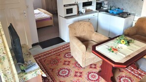 Quarto compacto com cama, cozinha compacta, sofá e uma pequena mesa com toalha de mesa florida.