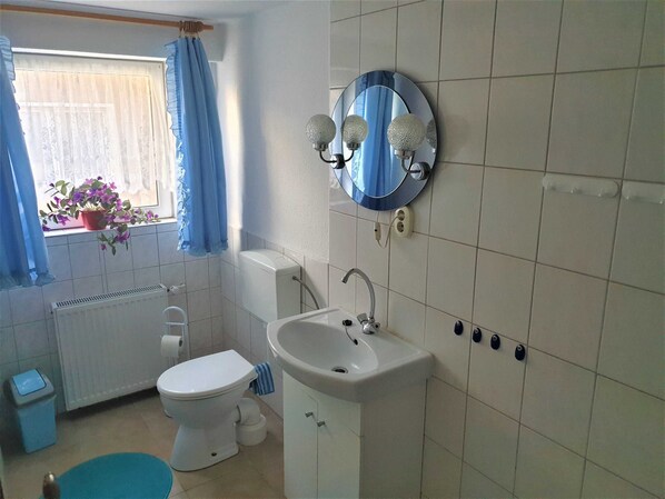 A bathroom with a toilet, sink, and a mirror with lights.