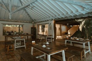 A rustic dining area with wooden tables and benches, a high ceiling with exposed beams, and a staircase leading to another level. - Pousada Erva Doce (Porto Seguro)