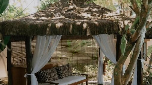 Une terrasse en bois avec un gazebo à toit de chaume, un banc et un petit étang.