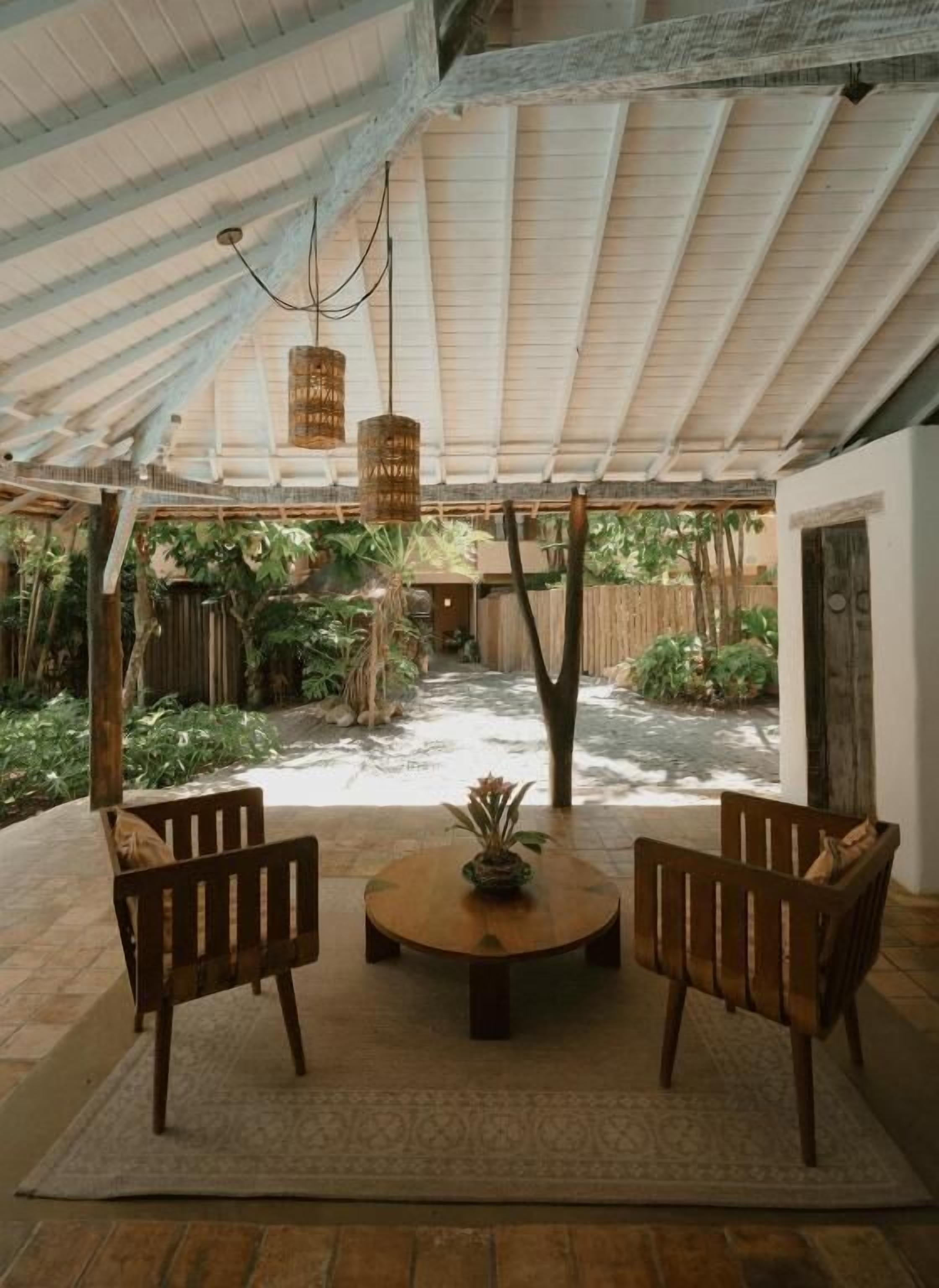An outdoor patio area with a round table, two wooden chairs, hanging lights, and a variety of plants.