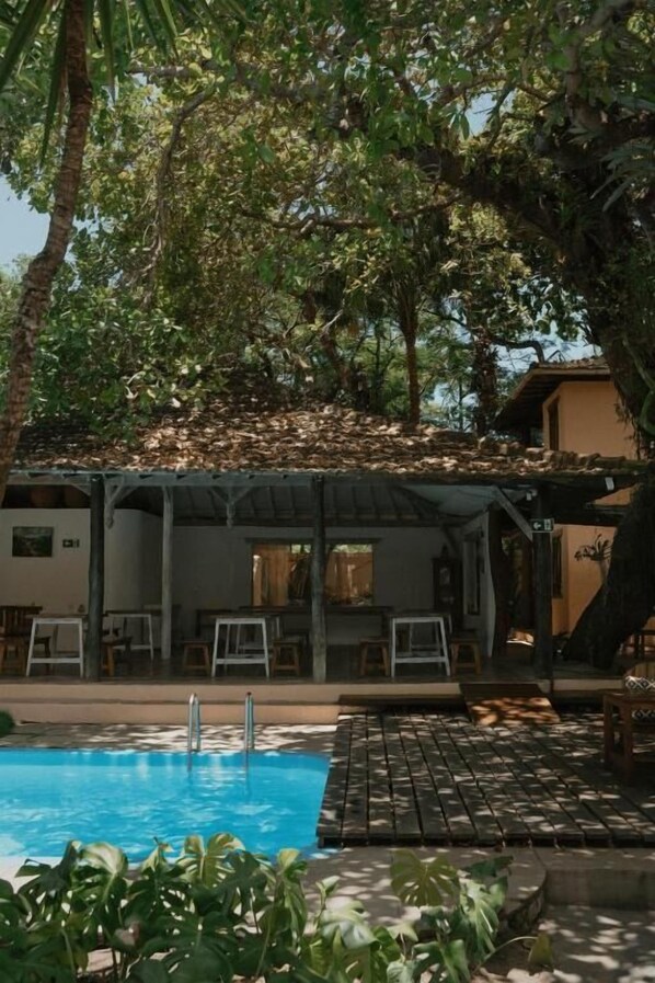 A pool area with a covered seating area and a building in the background.