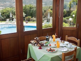 Una mesa de comedor con alimentos para el desayuno, vista a una piscina y mobiliario para exteriores.