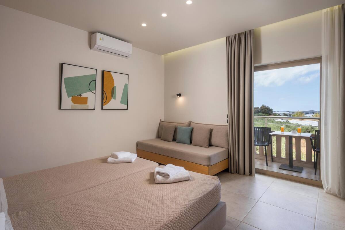 A hotel room with a bed, a sofa, and a balcony with a table and chairs.