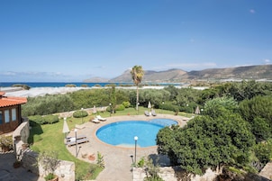 Una piscina rodeada de vegetación, con vistas al mar y colinas al fondo.