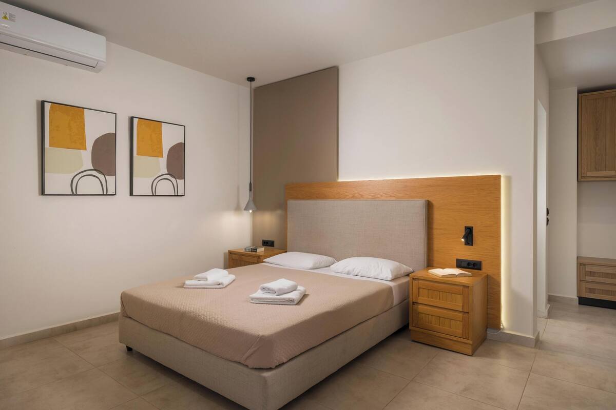 A neatly arranged bedroom with a bed, bedside tables, a nightstand, and a wooden headboard.