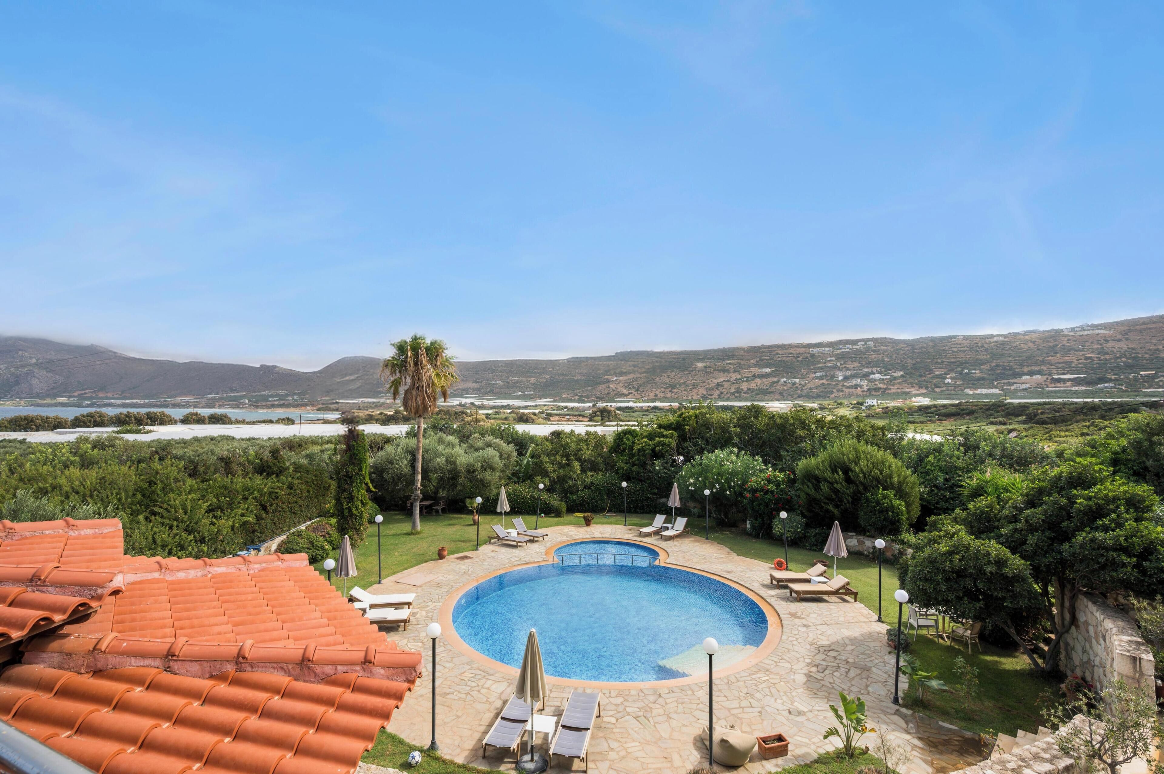Piscina com deck de pedra, rodeada por vegetação e vista para colinas distantes.