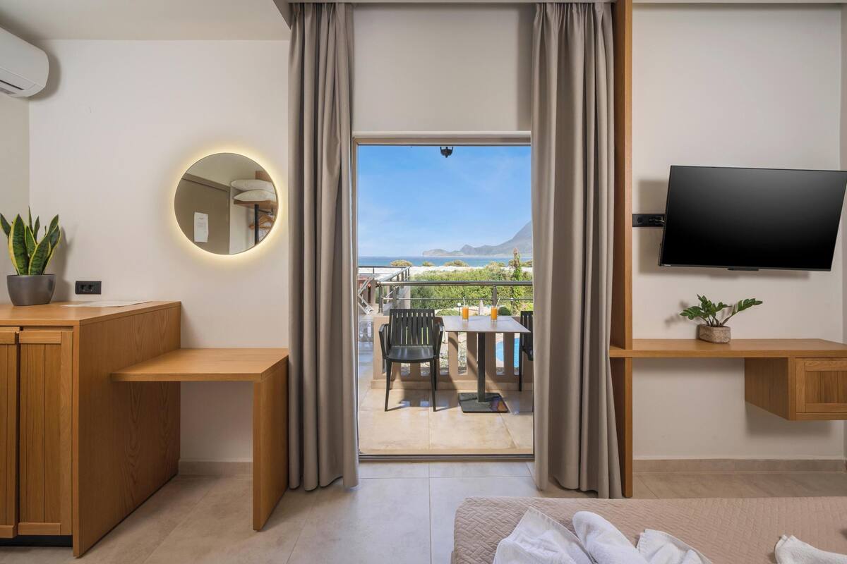 A modern hotel room with a balcony, a round mirror, a TV, and a wooden desk.