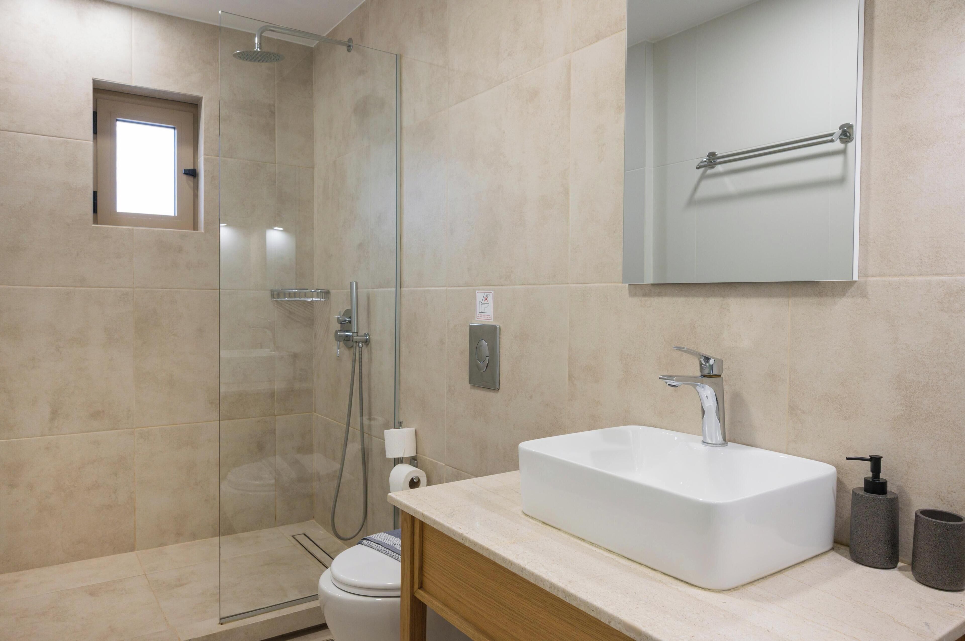 A modern bathroom with a glass-enclosed shower, a white sink with a soap dispenser, and a towel rack above the mirror.