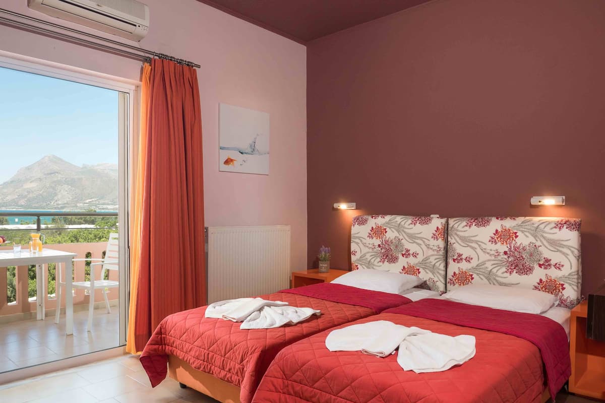 A bedroom with two beds, a view of mountains, a table with chairs, and a window with curtains.