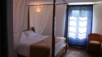Een hemelbed met gordijnen, een stoel en een raam.