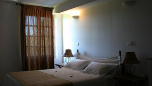 Ein Schlafzimmer mit einem Bett, zwei Nachttischlampen, einem Fenster mit Vorhängen und einer Wandleuchte.