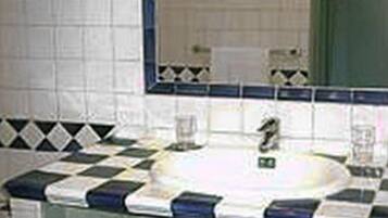Un baño con un lavamanos blanco, baldosas azules y blancas a cuadros, un espejo y una cesta de mimbre.