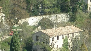 Um edifício com parede de pedra e telhado de telhas, rodeado por árvores e carros estacionados.