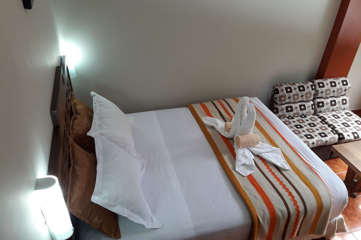 Une chambre d’hôtel avec un lit, des oreillers, une couverture à rayures et une chaise à motifs.