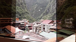 A view of a town nestled in a valley with buildings and a prominent mountain in the background. - Hostal Vista Waynapata (Machu Picchu)