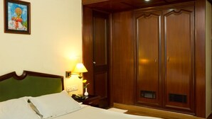 Een hotelkamer met een bed, nachtkastje, lamp, garderobe en een schilderij aan de muur.