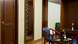 Een kamer met een houten deur, een spiegel met decoratieve lijst, een blauwe stoel, een klein tafeltje met een vaas en een afstandsbediening.