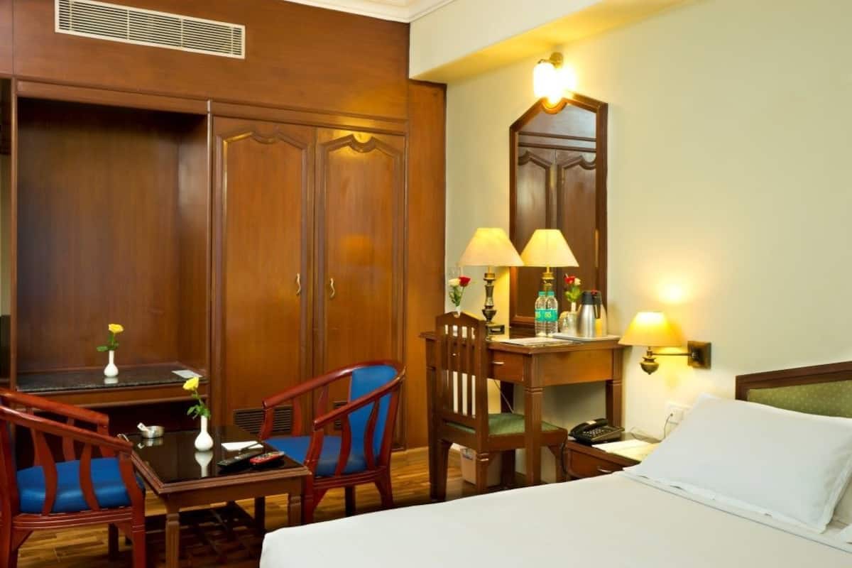 Een hotelkamer met een bed, twee stoelen, een klein tafeltje, een bureau, een spiegel en twee wandlampen.