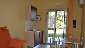 A compact room with a kitchenette, a dining area with a table and chairs, and a sliding glass door leading to an outdoor area. - La Marina residence club (Pietrapaola)