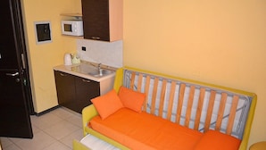 A compact room with a bed, a small kitchenette, and a door. - La Marina residence club (Pietrapaola)