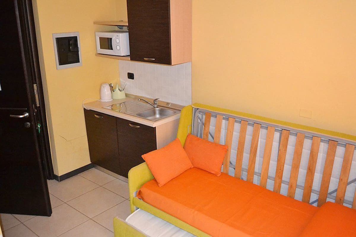 A compact room with a bed, a small kitchenette, and a door.