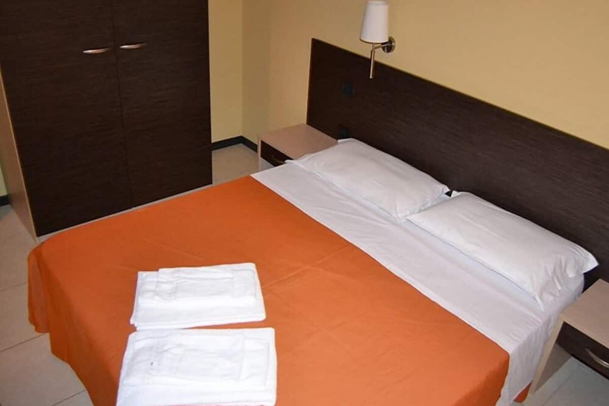 A hotel room with a bed, a nightstand, a lamp, and a wardrobe.