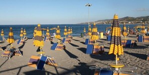 A beach with rows of sun loungers and umbrellas, a clear sky, and a distant view of hills. - La Marina residence club (Pietrapaola)